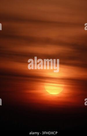 Dramatic golden sunset glowing through horizontal clouds over moody orange sky Stock Photo
