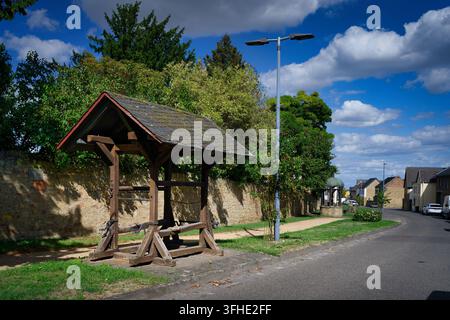 Historic wooden shoeing stock alongside a stone wall and street in Buervenich with a well in the background under a blue sky Stock Photo