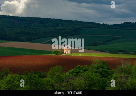 Historic windmill standing in rolling agricultural landscape among dark red crimson clover and green fields under a dramatic sky in Kunkovice, Czechia Stock Photo
