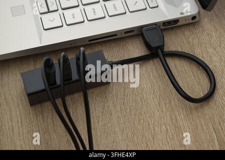 Close-up technical view of a black USB multi-port hub connected to a slim laptop, highlighting hardware connectivity, data transfer, and peripheral ma Stock Photo