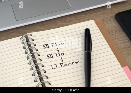 Close-up view of an open notebook featuring a hand-drawn management workflow schema with "Plan", "Do", and "Review" steps, accompanied by a sleek blac Stock Photo