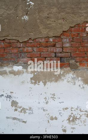 Deteriorating white painted concrete and red brick masonry wall with cracked paint, crumbling concrete, exposed brickwork Stock Photo