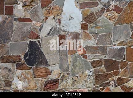 Multi-color machine-cut veneer stone and recessed mortar wall surface with three triangular stones forming a geometric arrangement Stock Photo