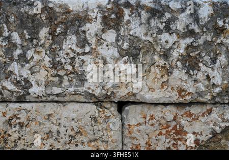 Sawn limestone retaining wall blocks with porous, rough faces in variegated gray, brown, and off-white tones, stacked in staggered rows Stock Photo