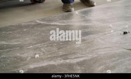 Floor tiling process with tile leveling system for precise installation. Construction site background shows focus on home renovation and skilled manua Stock Photo