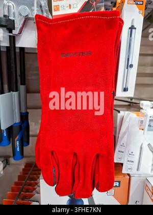 Denia, Spain - October 10, 2025. Bright red Dexter heavy duty heat resistant welding gloves are on display in a Spanish hardware store. They are desig Stock Photo