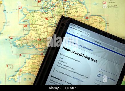 GOV.UK driving-test booking page on a tablet over a map of Wales & England amid continuing delays and frustration securing practical test appointments Stock Photo