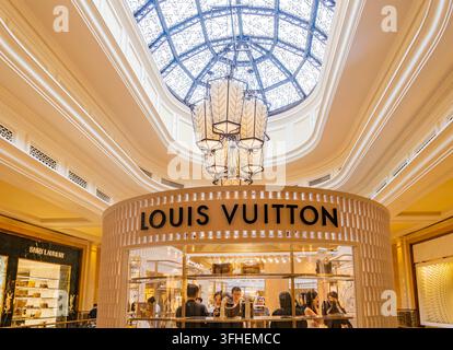 Macau, China, APR 16, 2024 - Customers browse a modern Louis Vuitton shop surrounded by gold accents and a grand ornate ceiling featuring an Stock Photo