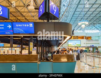 Travelers stand in line at a United Airlines check-in counter beneath a large blue gate number sign inside a spacious airport terminal. Stock Photo