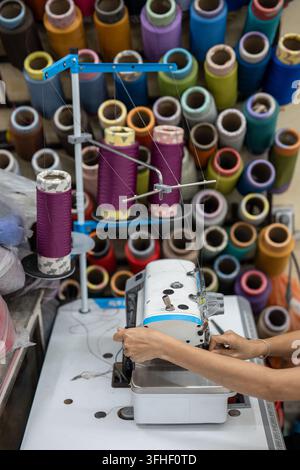 Weaving production in Vietnam, female seamstress hands operating sewing machine in workshop. Stock Photo