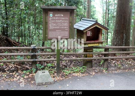A wooden information board stands next to a miniature wooden pilgrimage stamp station box behind a timber fence alongside a paved trail at Hosshinmon- Stock Photo