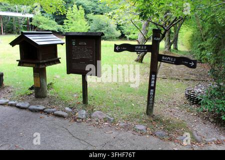 A brown multi-directional signpost pointing toward Fushigami-oji and Hosshinmon-oji stands alongside a wooden information board and a stamp station bo Stock Photo