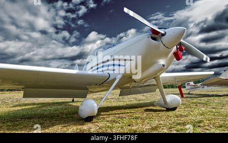 White light aircraft parked on a grassy runway with its propeller showing, dark clouds gathering above, indicating changing weather Stock Photo