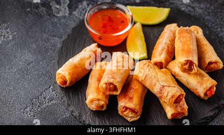 Fried spring rolls served with sauce and lime on a black plate Stock Photo