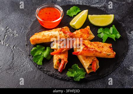 Fried spring rolls with shrimps served with sauce and lime on a black plate Stock Photo