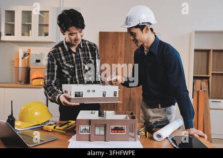 Asian architect and engineer team checking architectural house model using measuring tape on the table at office studio. Stock Photo
