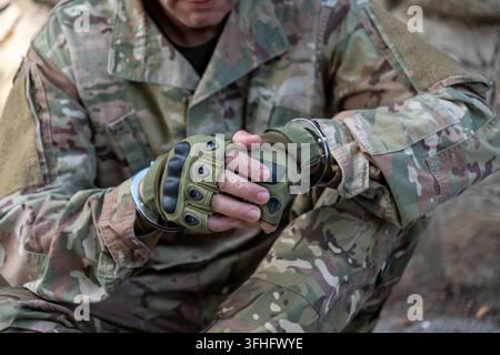 Detained serviceman in camouflage uniform sits with his hands restrained by metal handcuffs while wearing protective tactical gloves Stock Photo