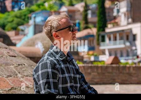 A handsome young blonde man of Caucasian appearance traveling in Tbilisi, Georgia, posing on the brick domes of the historic sulfur baths in the old t Stock Photo