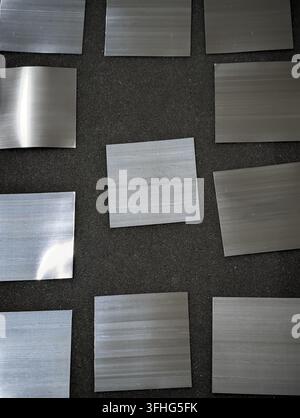 Several brushed metal sample squares in silver and gray tones are arranged across dark textured fabric, creating industrial texture contrast, material Stock Photo
