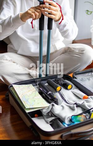 Woman inserts trekking poles vertically into suitcase already packed with essential hiking gear. Concept of outdoor equipment preparation and trip pac Stock Photo