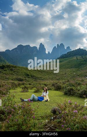 Man resting head on woman's lap in wildflower meadow below karst peaks, Nui Ngu Chi Son, Vietnam Stock Photo
