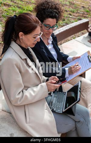 Businesswomen collaborating outdoors using technology and documents Stock Photo