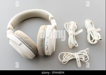 White overear headphones and various cables are neatly arranged on a gray surface Stock Photo
