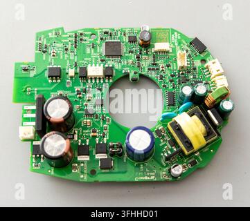 A green circuit board with chips and capacitors sits on a grey background Stock Photo