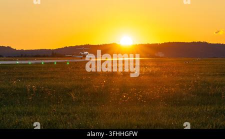A business jet on the runway with the sun setting directly behind it over distant hills Stock Photo