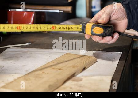 Close-up of a hand using tape measure to calculate dimensions of timber plank in a woodshop, highlighting professional measurement process for constru Stock Photo