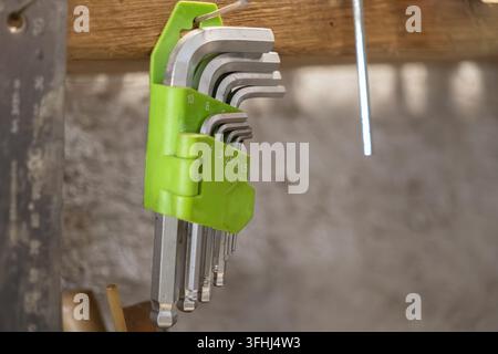 Metal Allen wrenches stored within a lime-colored rack suspended on a rough lumber surface, representing industrial repair readiness, tidy tool manage Stock Photo