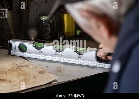 An experienced carpenter checks for flatness using a metal bubble level tool on a wooden surface, highlighting quality craftsmanship and meticulous at Stock Photo