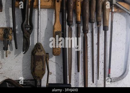 Various aged metal and wooden tools suspended upon a weathered wall inside a workshop, reflecting timeless dedication to skilled craftsmanship, manual Stock Photo
