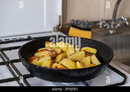 Crispy fried potatoes cooking in a heavy black pan over a gas burner to create a hearty home meal that captures the nostalgic essence of authentic com Stock Photo