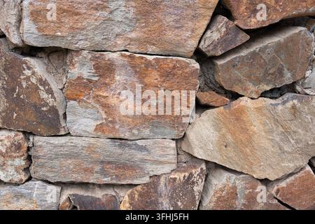 Natural stone wall with various shaped rocks and stones cemented together, creating a rugged and earthy texture for architectural and decorative backd Stock Photo