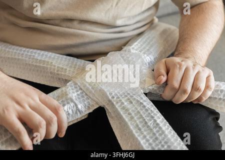 An individual securely packing wooden chair parts with plastic bubble wrap, demonstrating careful preparation for safe transport during a domestic mov Stock Photo