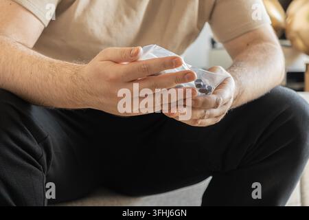 Close up on a person holding a bag of dark supplements or medicinal tablets, capturing an essential moment of care in a household setting to prioritiz Stock Photo