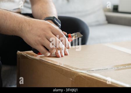 Person carefully slicing through packaging tape on a delivery carton with a razor cutter, demonstrating a practical approach to opening freight during Stock Photo
