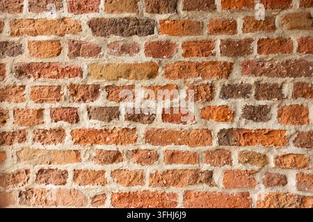 Close-up of a weathered red and orange brick wall with rough masonry texture, uneven surfaces and light mortar joints, forming a rustic architectural Stock Photo