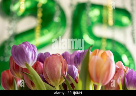 Vibrant spring tulips in shades of soft purple and peach stand out against a bokeh backdrop of shiny green balloons, creating a cheerful aesthetic for Stock Photo