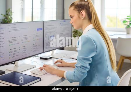 Businesswoman Using AI Dashboard on Dual Monitors in Bright Office Workspace Stock Photo