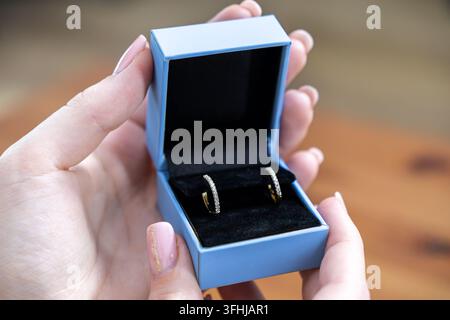 Small diamond hoop earrings rest inside an elegant open box held by hands with manicured nails, representing a thoughtful gift choice for celebration, Stock Photo