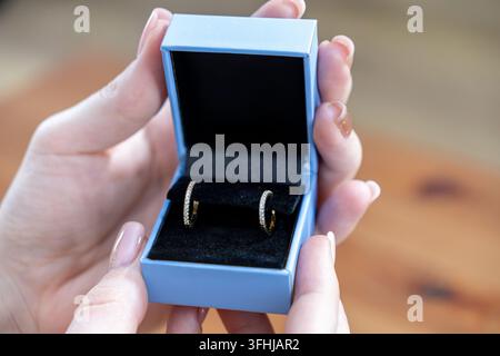 Hands hold open a boutique jewel case with sparkling gold earrings inside, conveying a sense of celebration, sophistication, premium quality, and prec Stock Photo
