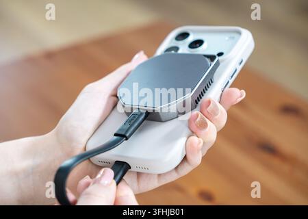 Hand holding a mobile phone connected to a compact external ssd, illustrating portable high-speed data transfer and convenient storage expansion for c Stock Photo