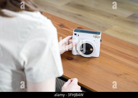 Person rests fingers near a sleek white instant camera on a rustic timber surface, embodying a creative lifestyle focused on tangible photography, art Stock Photo