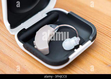 Modern hearing aid device sits within an open black plastic container placed on a desk, representing professional medical technology for auditory reha Stock Photo