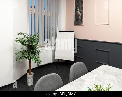 An empty meeting room with a clean whiteboard easel stands against a dual tone wall, reflecting a tidy environment for small business discussions, cre Stock Photo