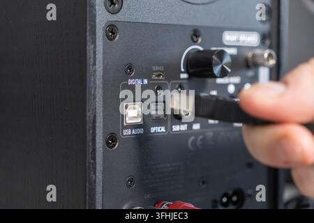 Close up of a human hand connecting a black cord into the input port of an active loudspeaker, demonstrating precise hardware configuration for high f Stock Photo