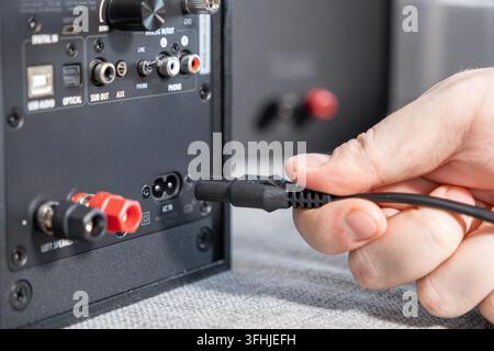 Close-up of a person connecting a black electrical cord to the back panel of a speaker system, illustrating technical maintenance or the assembly of q Stock Photo