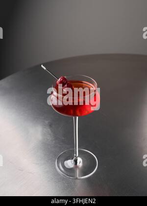 Close up of crimson cocktail in curvaceous coupe glass with cherry garnish on reflective metal table, with cocktail, red, drink, glass detail, showing Stock Photo